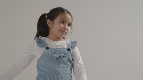 Studio-Portrait-Of-Bored-Hyperactive-Girl-Swinging-Arms-Against-White-Background