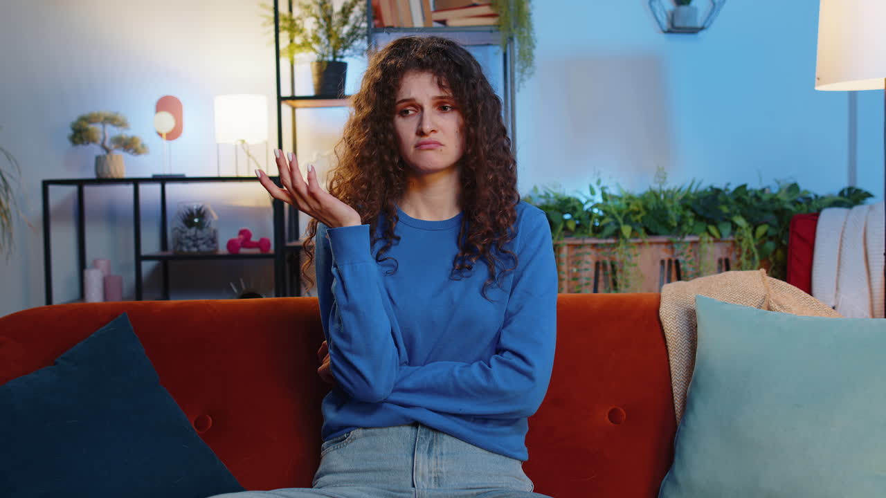 Upset bored lonely young woman girl thinking about problems sitting on home sofa annoyed burnout