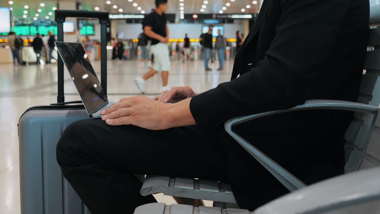 Businessman Uses Laptop, Waiting for a Flight in Airport Terminal or train station, Traveling Entrepreneur Working Online On Computer Sitting in a Boarding Lounge of Airline Hub with Airplanes