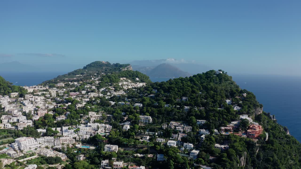 Vista aerea con drone di una città collinare sull'isola di Capri con edifici bianchi su ripide scogliere rocciose. Famosa isola calcarea nel Mar Mediterraneo lungo la costa italiana in una soleggiata giornata estiva.