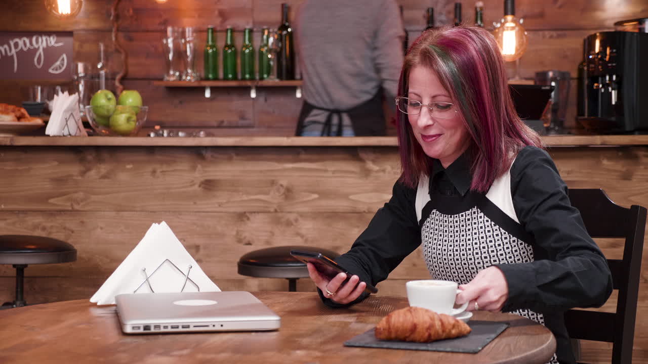 Woman in cafe using mobile phone with croissant and coffee on the table