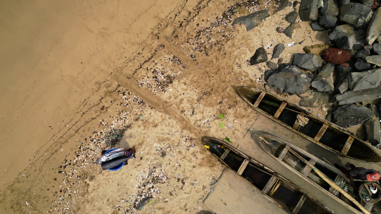 Top down aerial above a person carrying swordfish on a beach in Sao Tome, Africa
