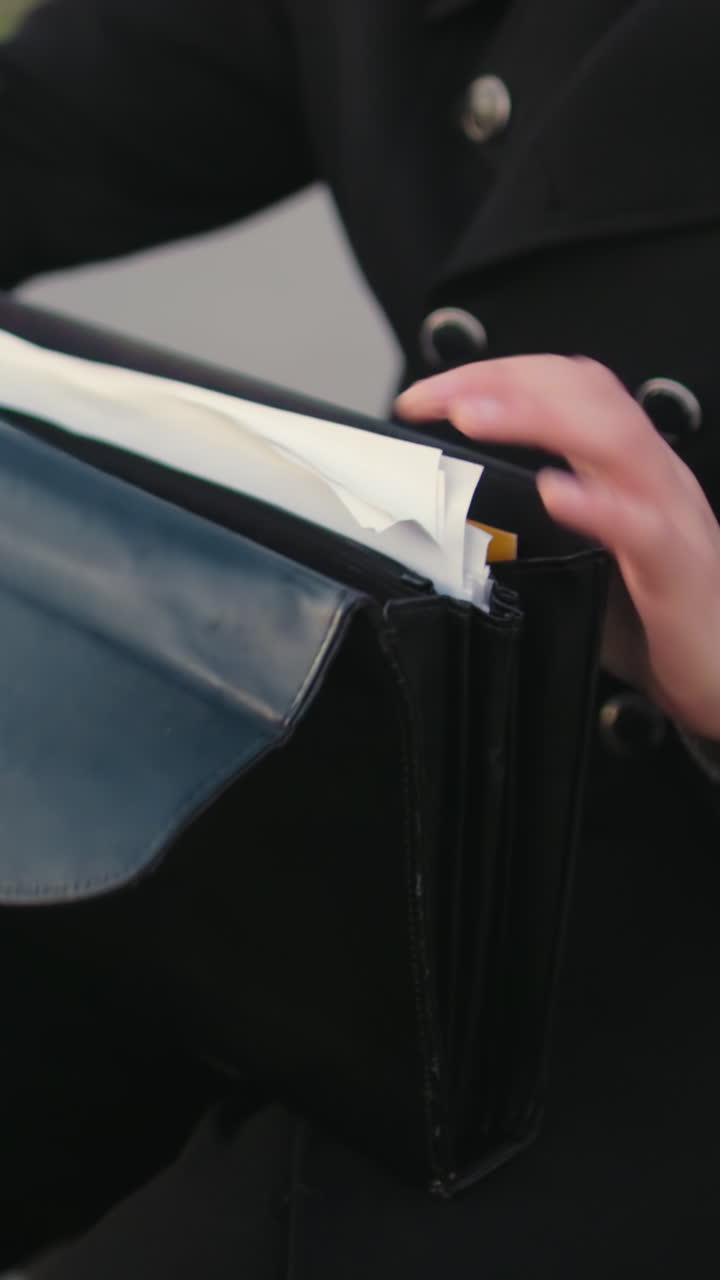 up de la mano individual en ropa negra pasando por los documentos en la bolsa, con el fondo con vegetación y camino entrelazado