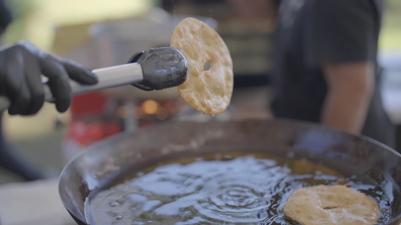 Close-up of torta frita being lifted out of hot oil with tongs, with steam rising as it’s raised. Simple shot emphasizes texture and cooking action. Perfect for food reels