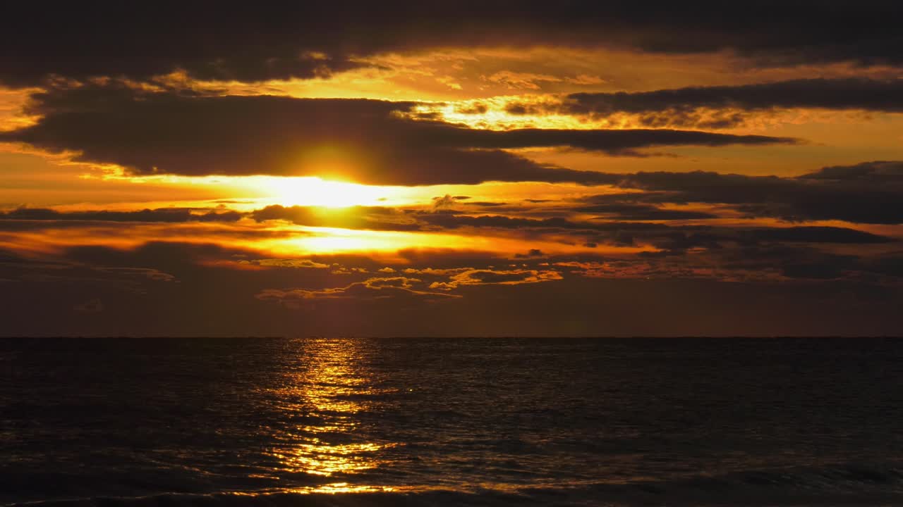 Golden sunrise in cloudy skies over dark ocean, seascape