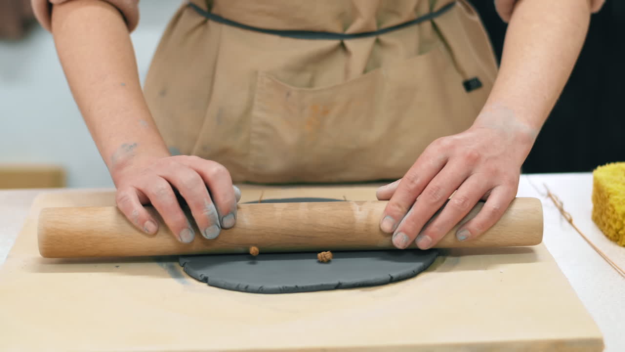 The master of sculpting pottery working in a studio. Compressing twigs into the clay with a rolling pin