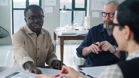 multi-etnische mannelijke architecten bespreken papieren met een vrouwelijke collega