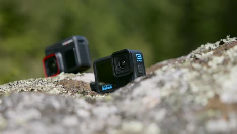 two action cameras sitting on outdoor rock background, detail close up