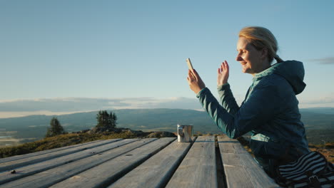 the traveler is talking on video chat sits at a table high in the mountains against the backdrop of