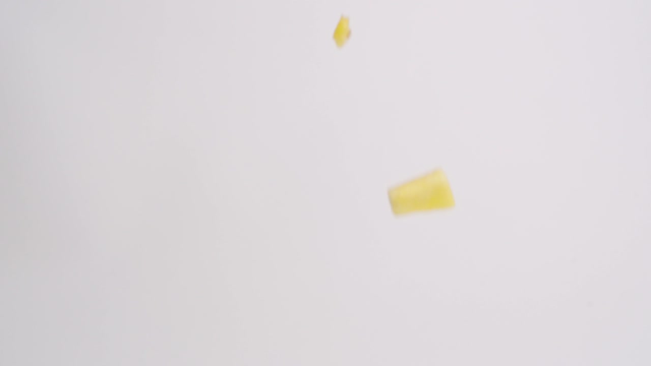 흰색 배경에 슬로우 모션으로 비가 내리는 밝은 노란색 파인애플 과일 큐브 조각