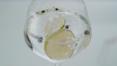 rebanadas de limón cayendo en un vaso con líquido transparente