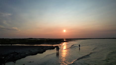 a drone shot of two people walking down the beach as the sun sets.