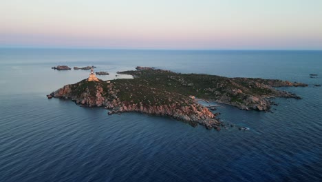 Lighthouse-on-small-island-during-sunset-in-Sardinia,-Italy---Aerial-4k