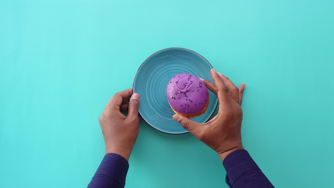 Person hält einen lila Donut auf einem blauen Teller