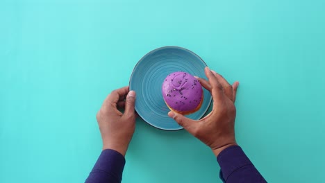 persona sosteniendo una rosquilla púrpura en un plato azul