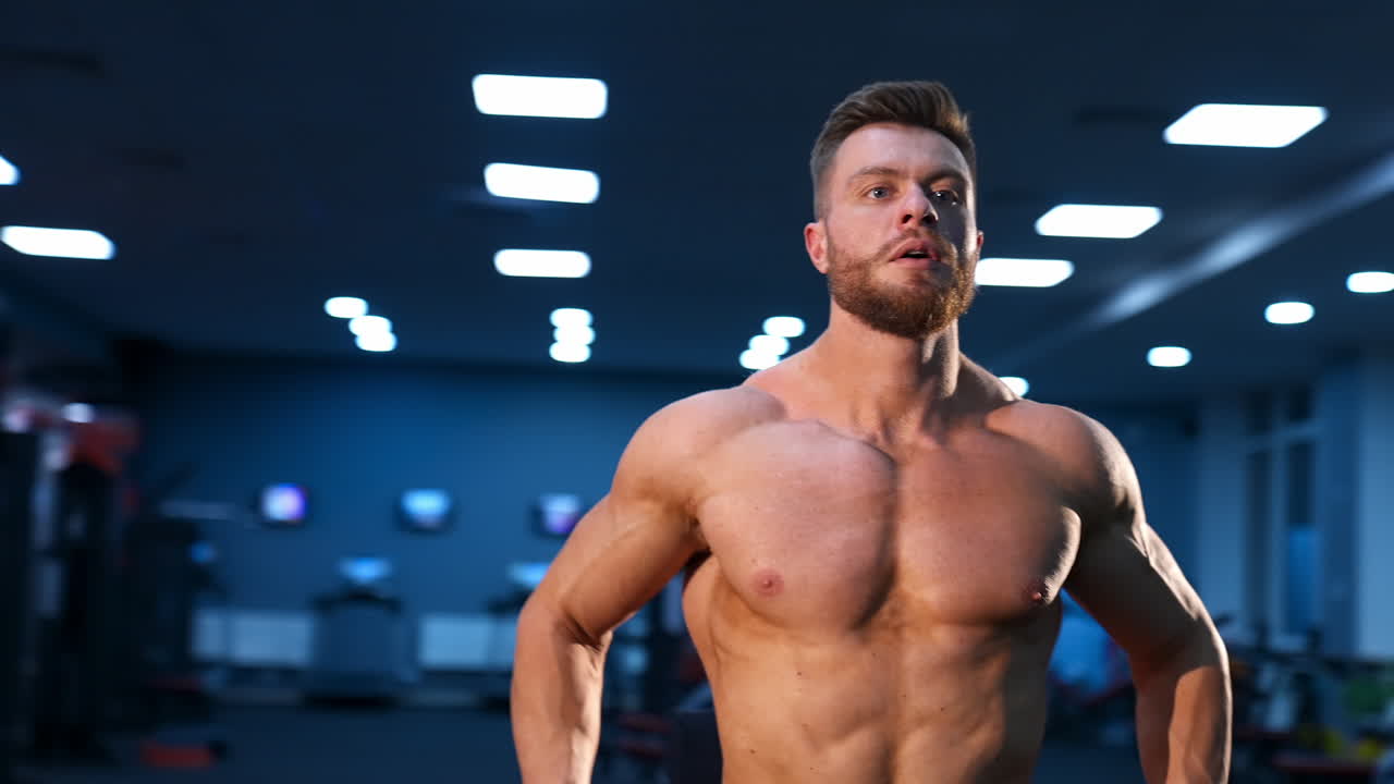 Athletic man in gym is posing to the camera. Bodybuilder with perfect body. Naked torso with perfect abs.