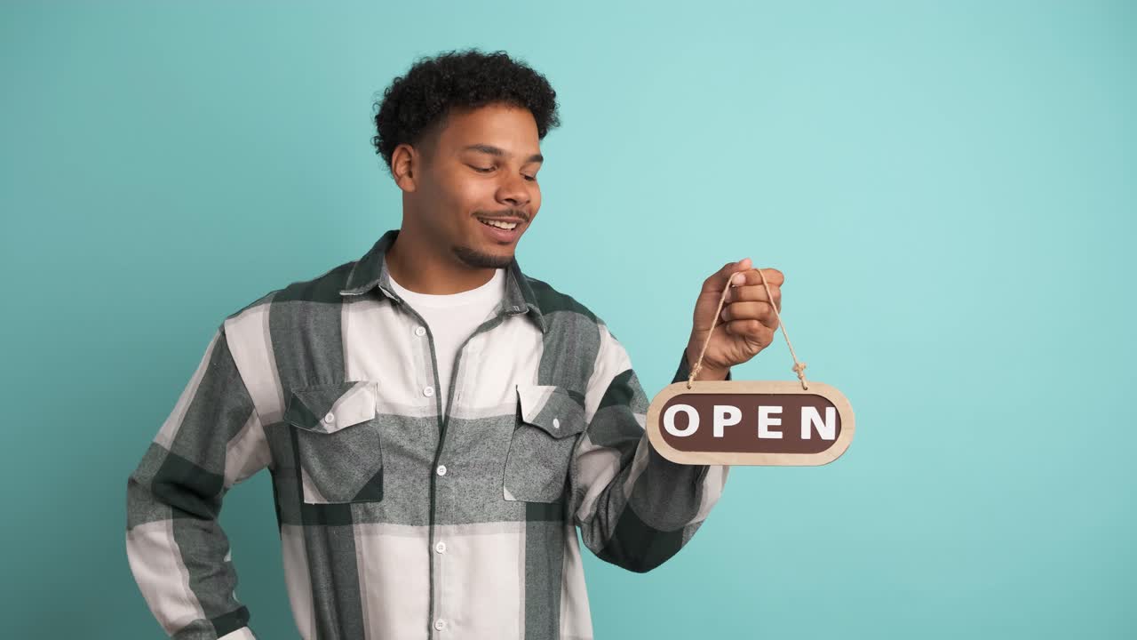Smiling man with open sign inviting in blue studio