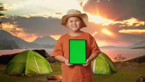boy holding tablet at campsite at sunset