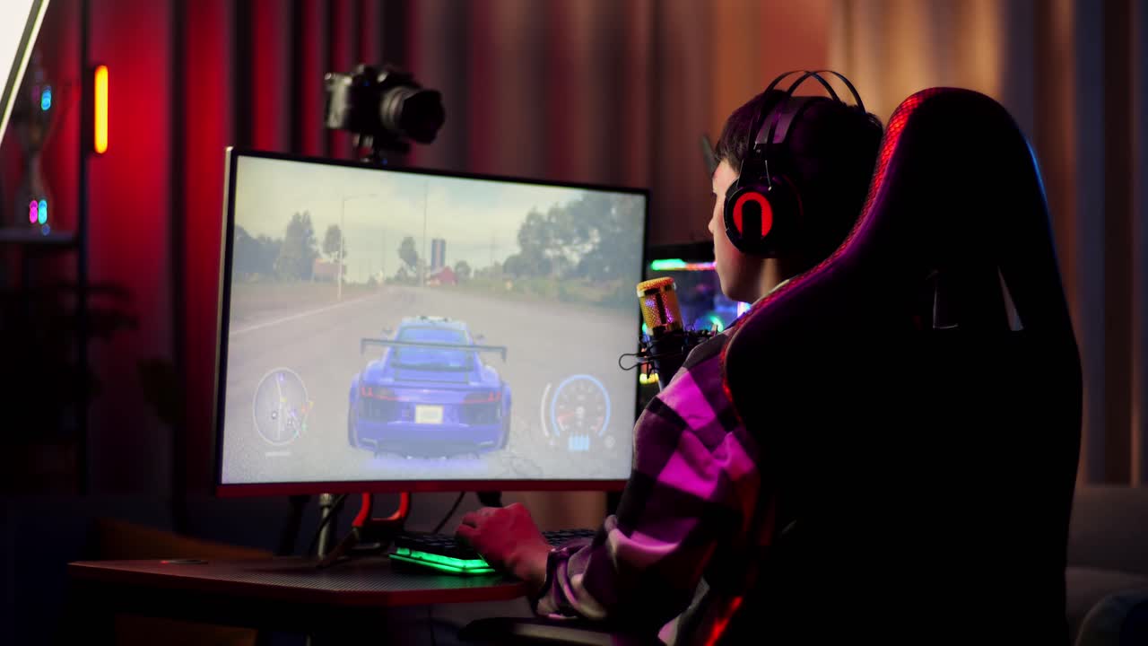 아시안 소년 스트리머가 컴퓨터에서 네트워크를 통해 자동차 레이싱 게임을하고 마이크에서 참가자들과 이야기하고 있습니다. 라이브 스트리밍 비디오 게임, rgb led 스트립 라이트에 의해 조명 된 책상