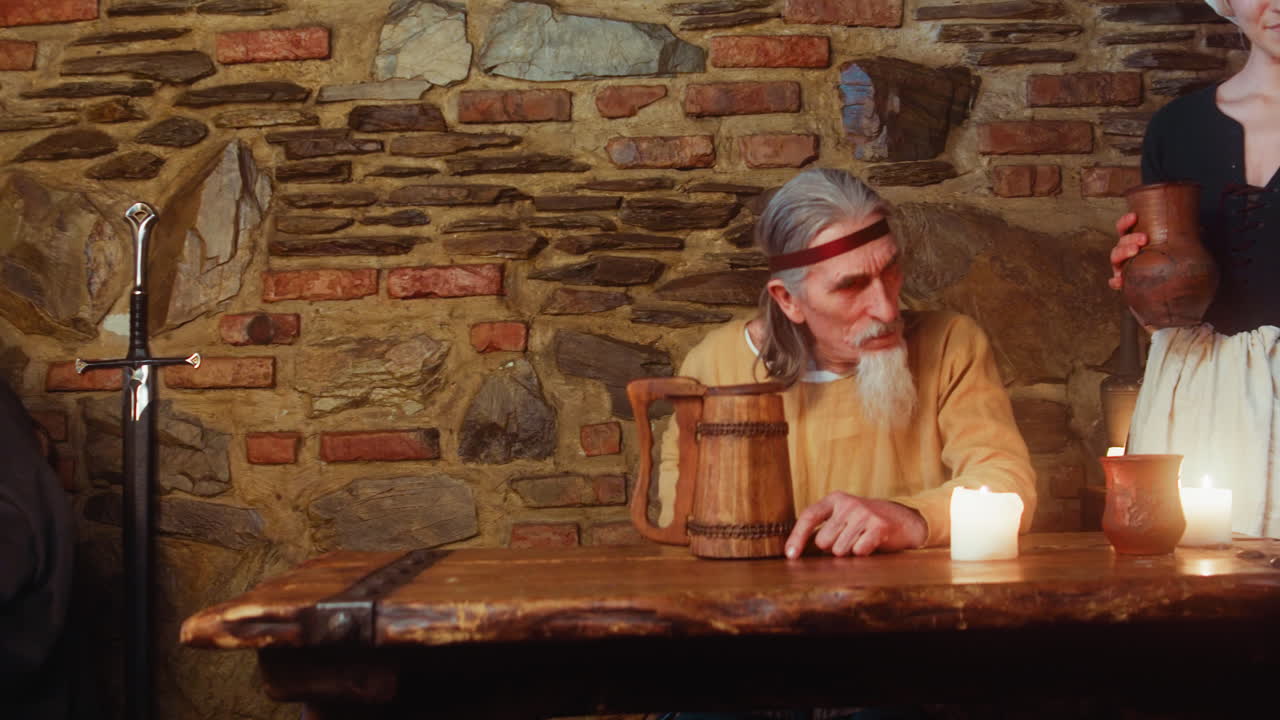 гости пьют за старым деревянным столом под контролем владельца таверны. персонажи фантастических сказок общаются, отдыхая в древнем пабе с красивой служанкой.