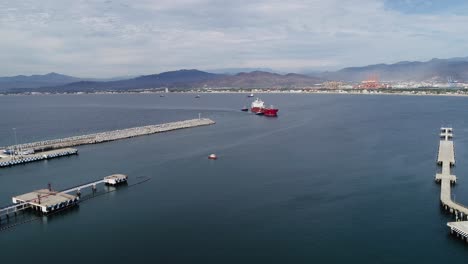 Vista-Aérea-De-Remolcadores-Que-Ayudan-A-Un-Carguero-Vacío-Al-Puerto-De-Manzanillo,-En-El-Nublado-México