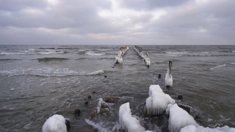 breakwater of old pier in ice with soft waves rolling at the baltic sea - wide shot, static