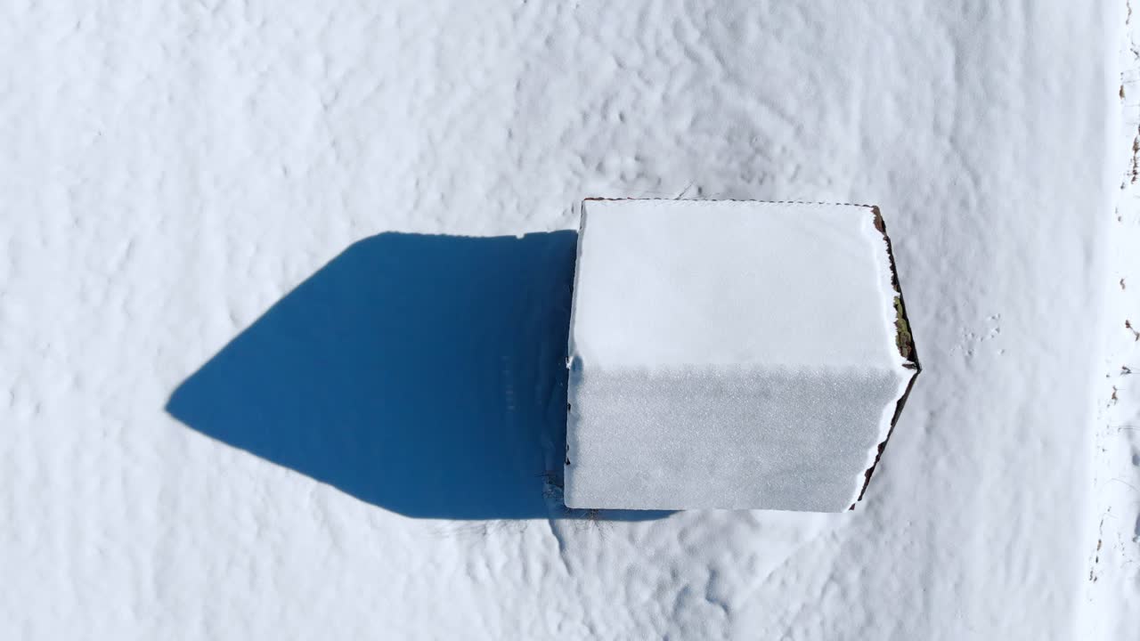 Aerial: zenital shot of a snowy cabin in the Alps in a sunny day