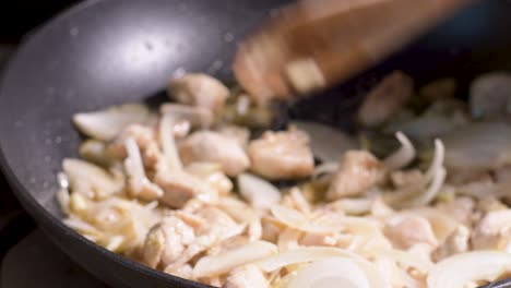 Stir-Fried-Chicken-With-Onions-cooking-in-Pan,-stirring-with-a-wooden-ladle,-close-up