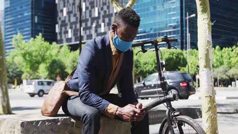 african american businessman wearing face mask texting on smartphone in street