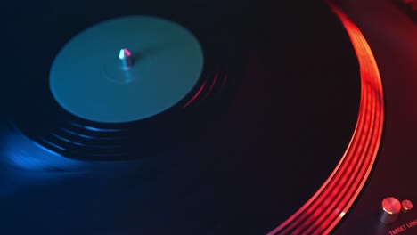 el tocadiscos de vinilo del reproductor en primer plano sobre un fondo de luces rojas y azules. la mano del joven coloca suavemente la aguja en la placa giratoria. dj en la fiesta de un estudiante joven