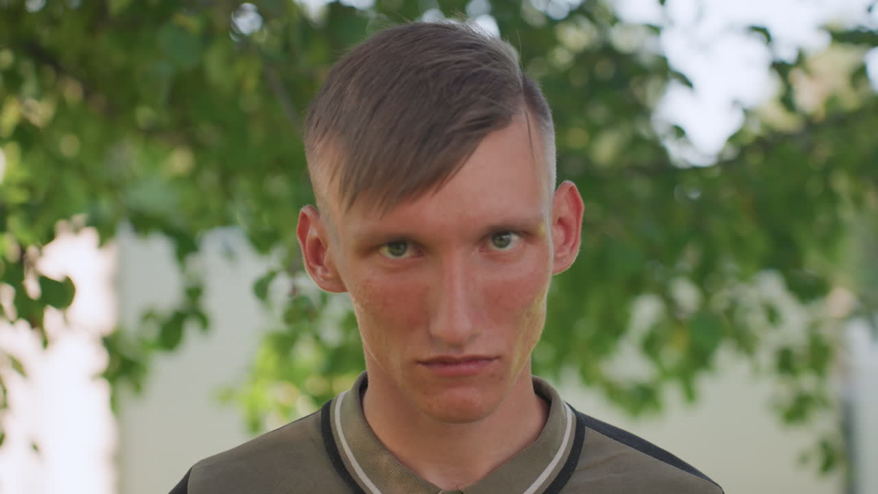 White Man Portrait Under Tree At Twilight, Pensive Expression And Soft Evening Light Create Melancholic Mood, Quiet Park Setting With Leafy Shadows, Introspective Moment Hinting At Paranoia