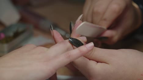 A-manicurist-filing-a-woman's-nails-in-the-beauty-salon,-hands-close-up,-bokeh-shot