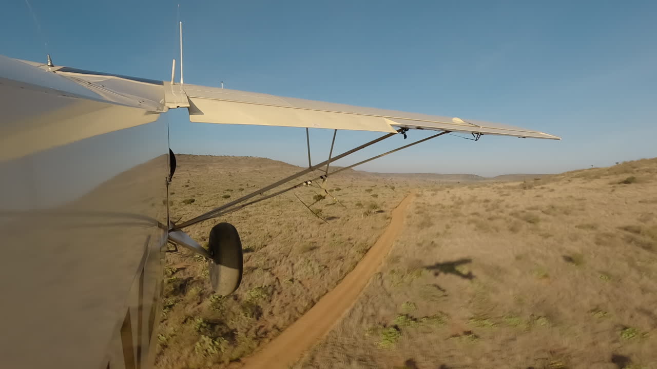 Seitenansicht eines kleinen Flugzeugs über Sträuchern, Straße und Hügeln