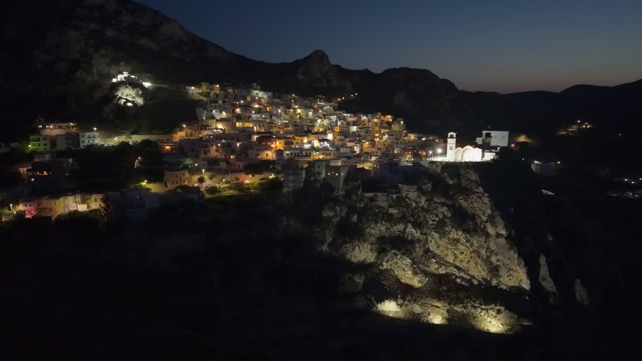 Aerial night drone footage of Menetes Village on Karpathos Island, Greece — showcasing its illuminated streets, colorful houses, and peaceful Mediterranean charm