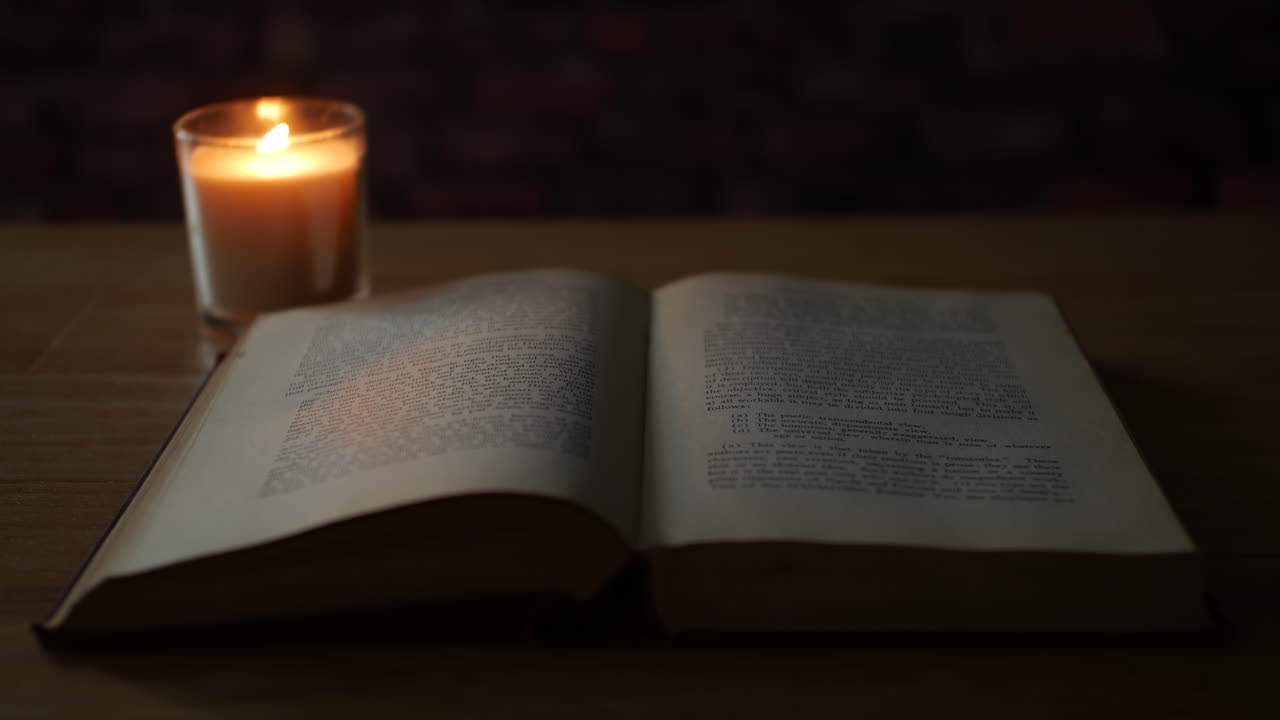 Старая книга на столе, освещенная мерцающей свечой в темной комнате.