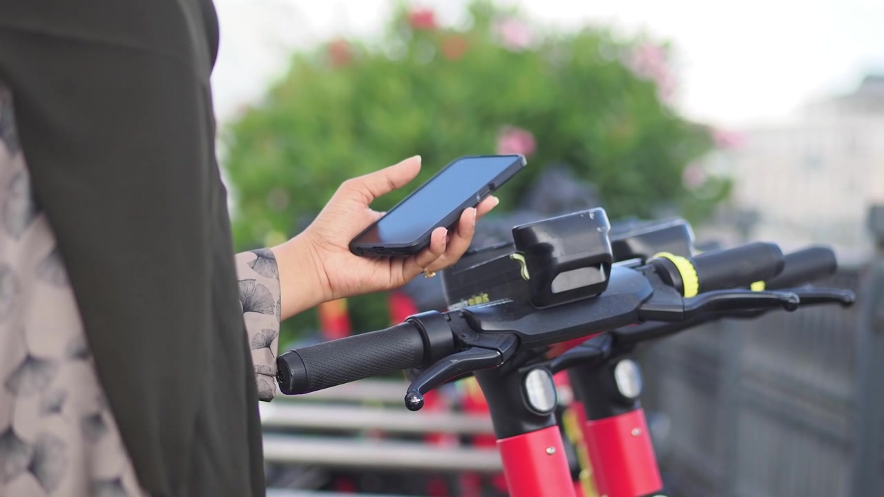 Žena používající chytrý telefon k odemknutí elektrické koloběžky ve městě