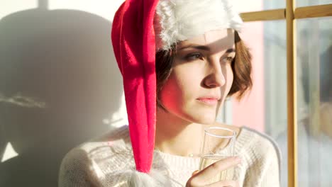una mujer con sombrero de santa bebiendo champán junto a la ventana.