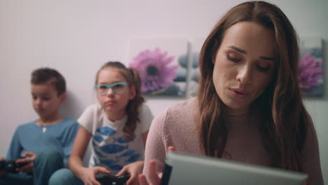 Happy-mother-looking-tablet-at-home-while-children-playing-in-video-games