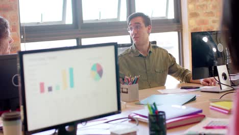 feliz caucásico creativo hablando con diversos colegas en el escritorio en la oficina casual, cámara lenta