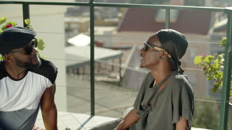 cheerful gay couple sitting on walk-out balcony and talking