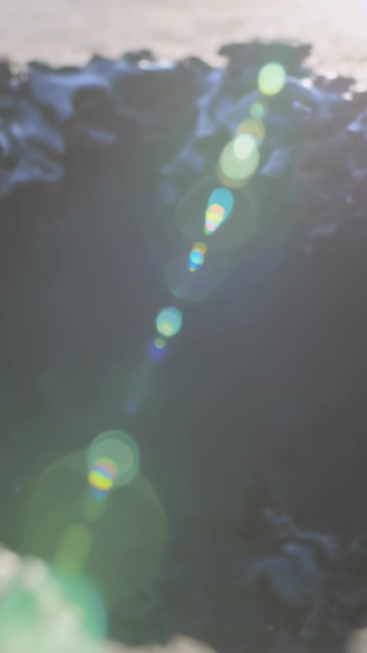 Vertical video: Tilting camera exposing green flare chain brightening at cliff top, finger entering