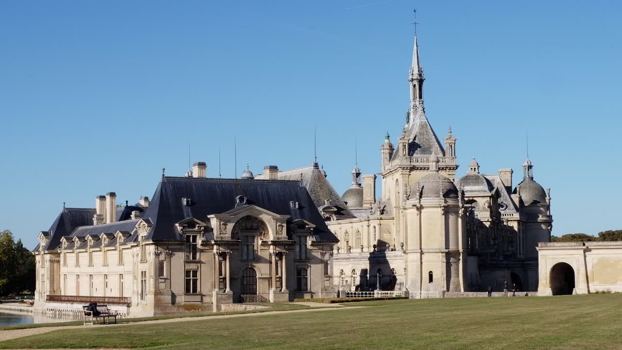 View of the Chateau de Chantilly castle surrounded by immense mirrors of water in Chantilly, Oise, France in daylight