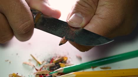 Footage-of-hands-slowly-sharpening-a-pencil-and-some-coloured-pencils-with-a-sharp-knife