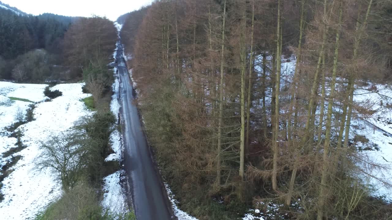 Snehvidt walisisk skovlandskab, Moel Famau vinterlandskab, luftfoto der daler ned mod højre over landevej.
