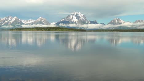 morning view of a very calm jackson lake in grand teton national park with the tetons in the background and very low clouds