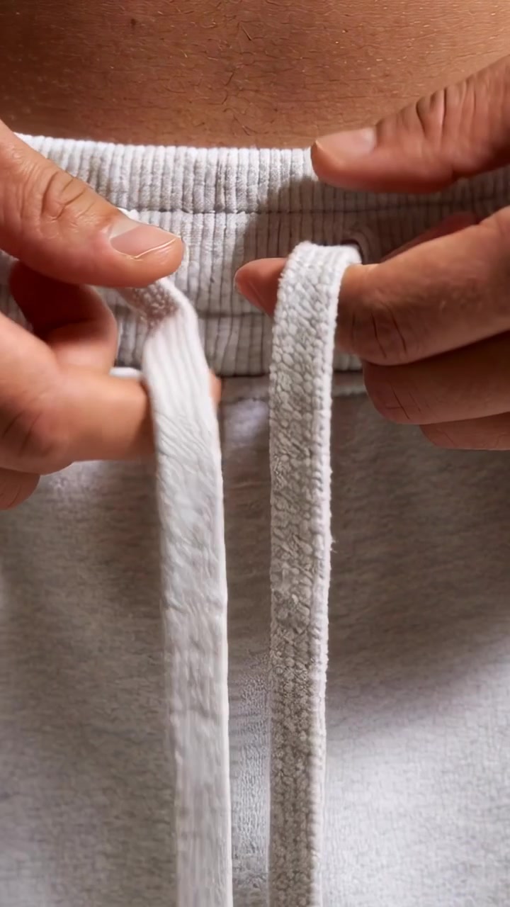Vidéo verticale : À la maison, une personne ajuste son pantalon gris en tirant et nouant les cordons à la taille.
