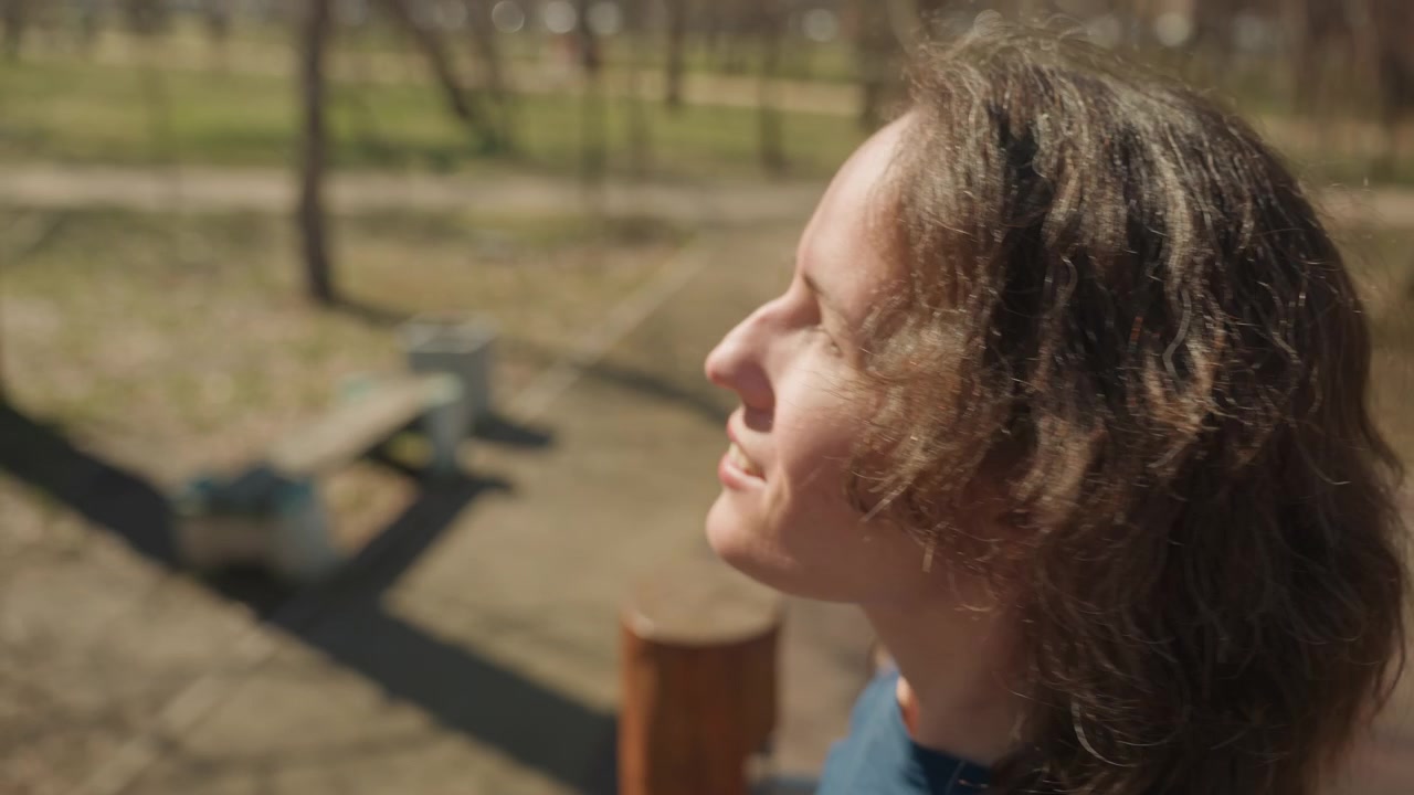 Primo piano di una giovane donna che si arrampica su un'attrezzatura da gioco in legno in un parco all'aperto. La donna si allunga e si aggrappa alla struttura indossando abiti casual, con la luce del sole che proietta ombre su di lei.