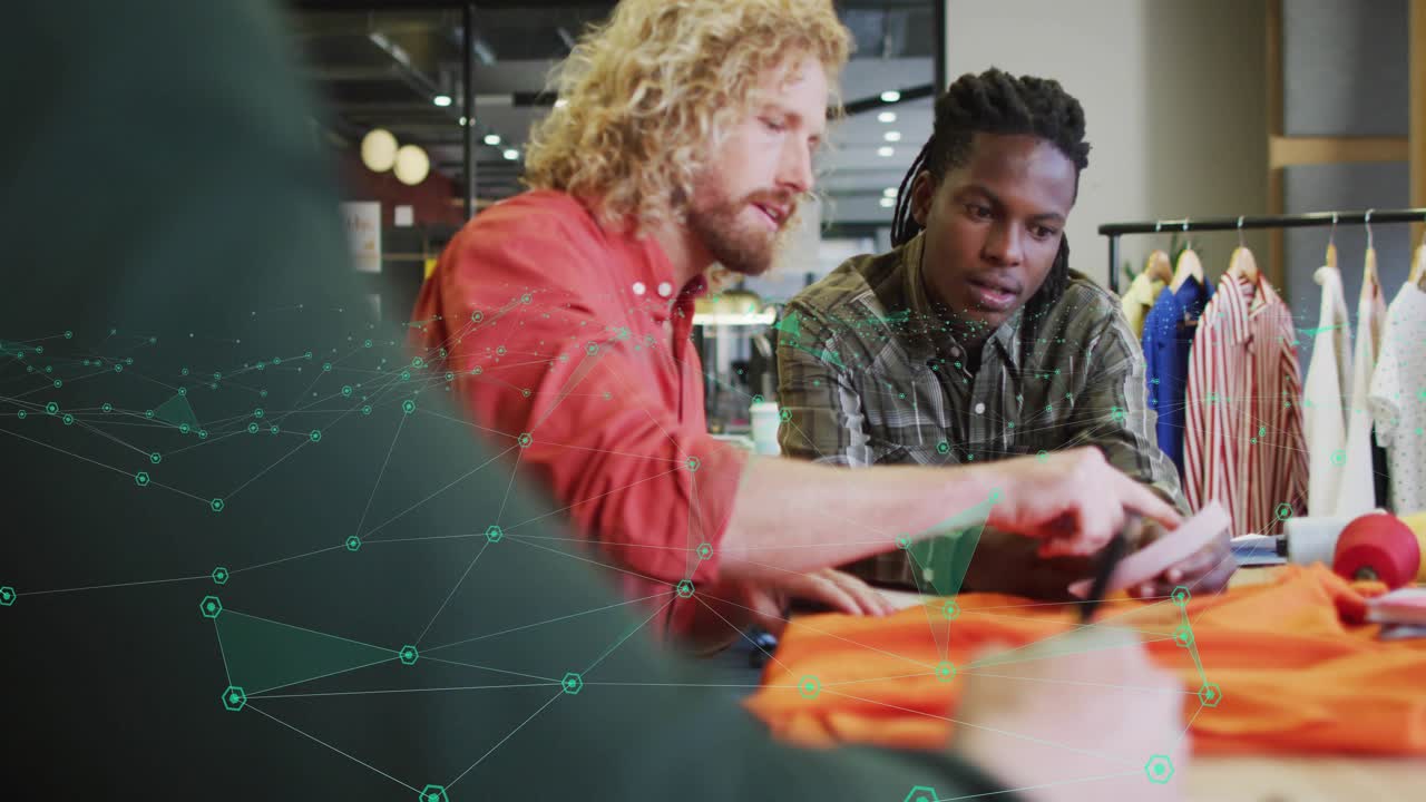 Two designers reviewing orange garment in fashion studio, tapping device and viewing green overlay