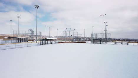 baseball and softball field covered in fresh powder snow during the day, aerial orbit