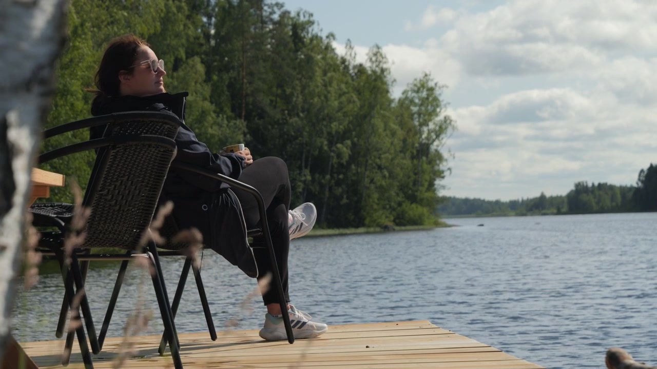 Suomalainen nainen rentoutuu puisella hetyllä nauttien pohjoismaisesta lomamaisemasta
